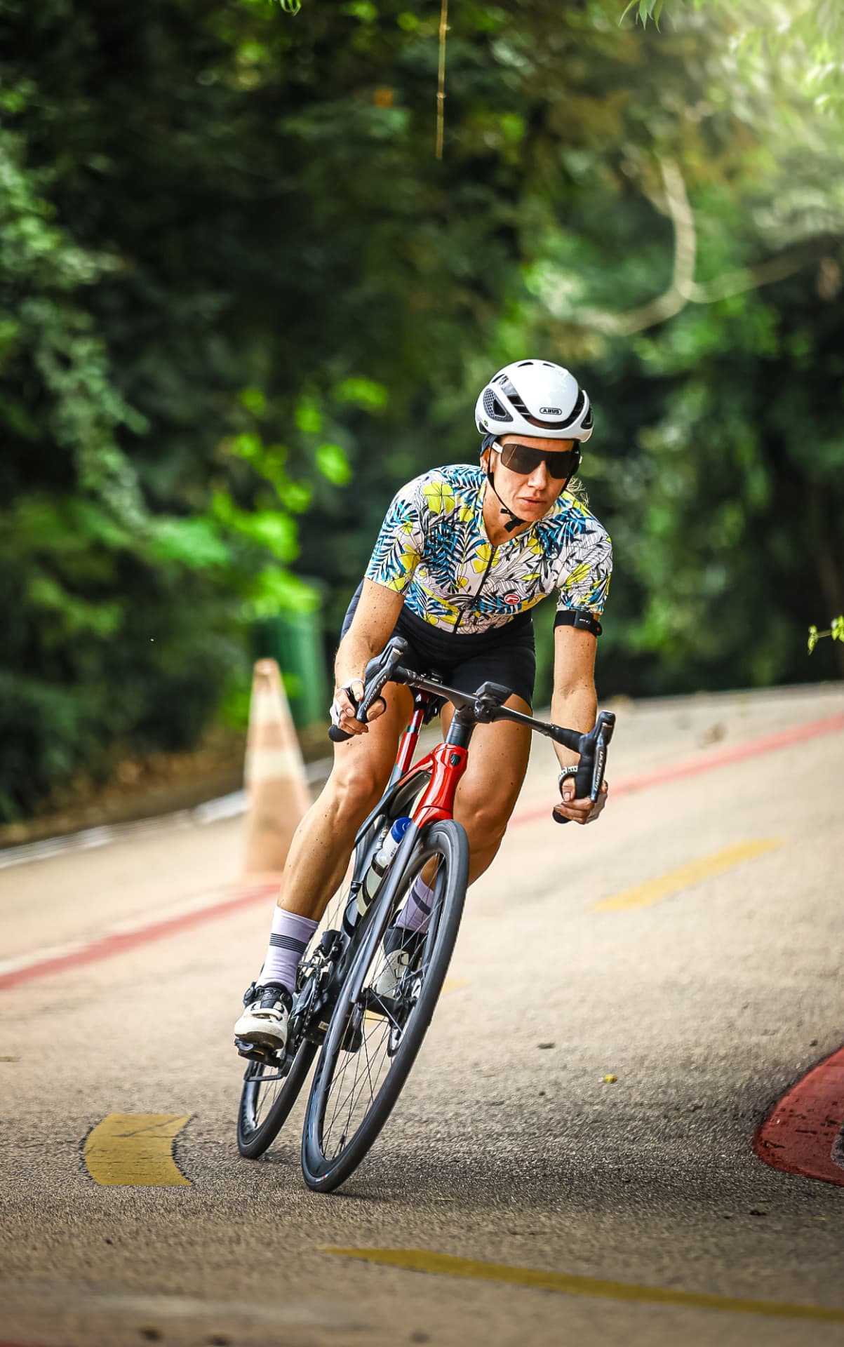 Ciclista de capacete branco em pista cercada por árvores